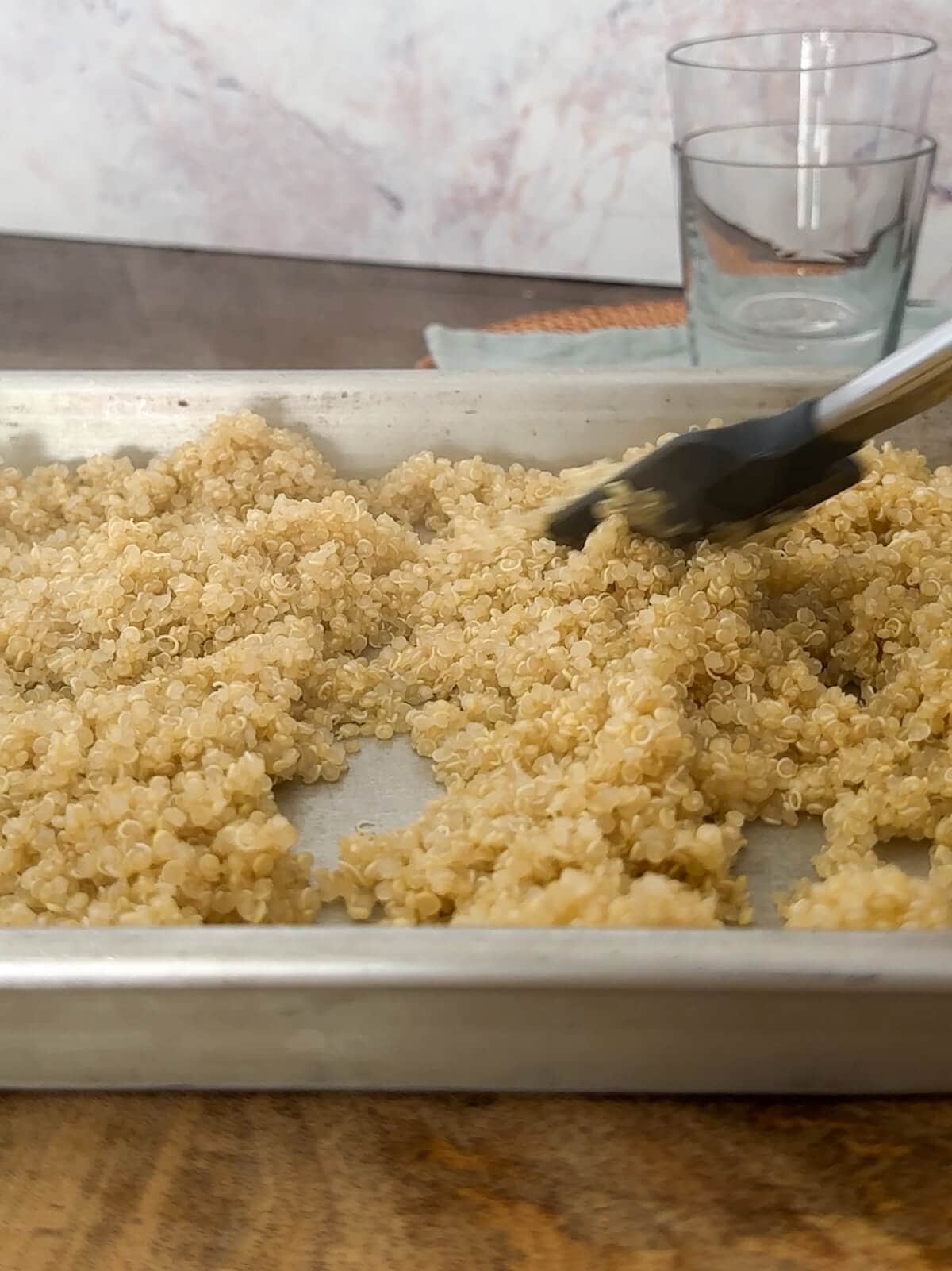 Spreading cooked quinoa on a baking sheet to cool quickly.