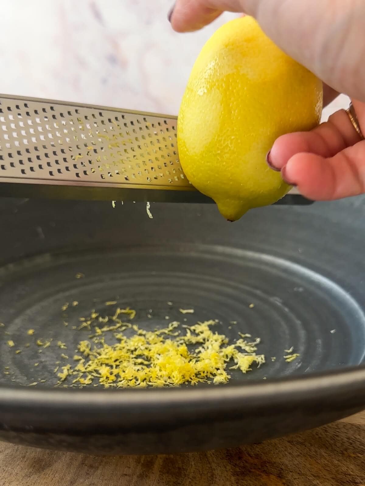 zesting a lemon over a bowl using a microplane grater.