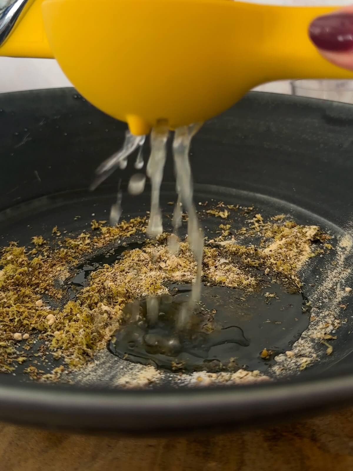 Adding lemon juice to bowl of spices for quinoa chickpea side dish dressing.