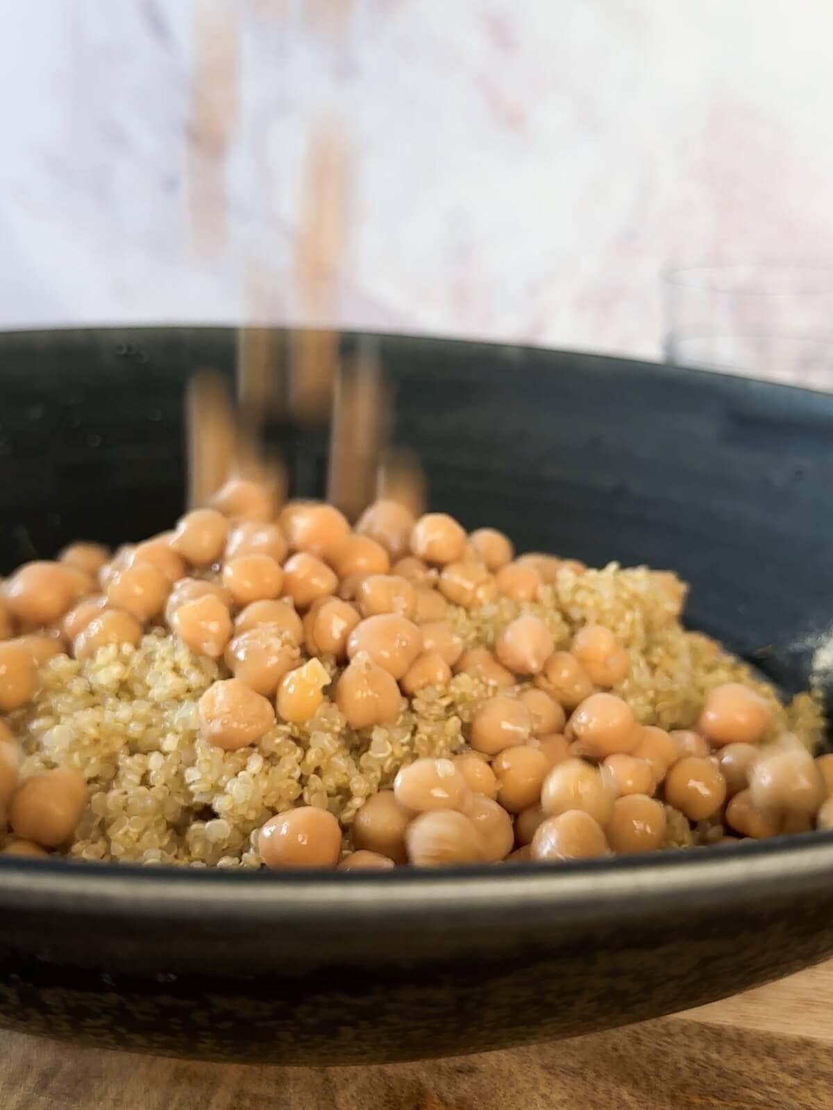 Mixing chickpeas and quinoa in a bowl with the salad dressing.
