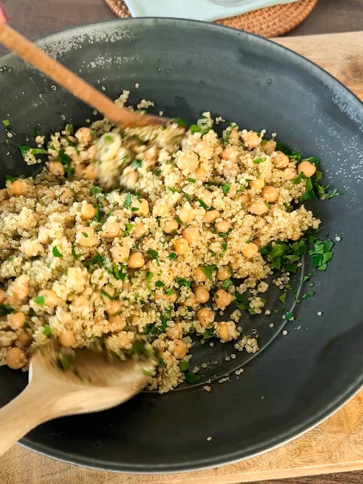 Tossing together quinoa, chickpeas, dressing, and parsley using wooden spoons to finish side dish.