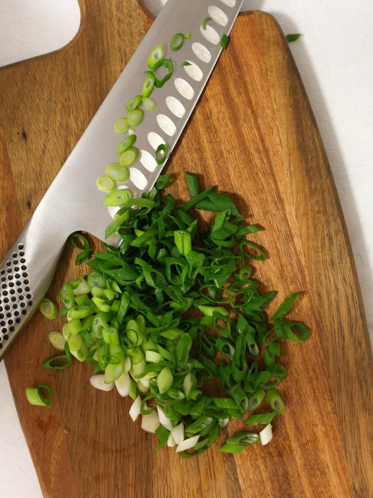 Sliced scallions on a board with knife.