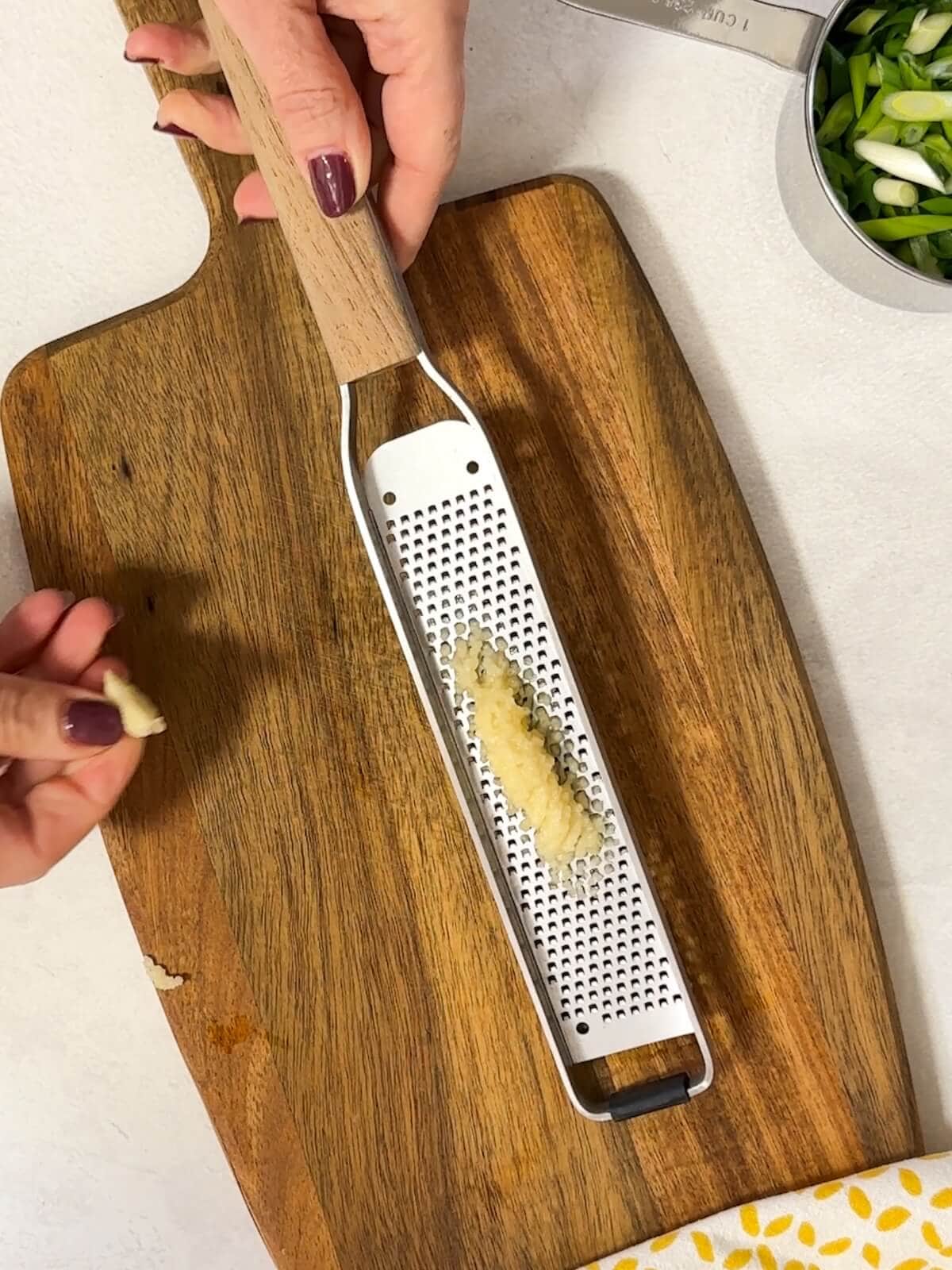 microplane grater with garlic cloves on a cutting board grating into puree action