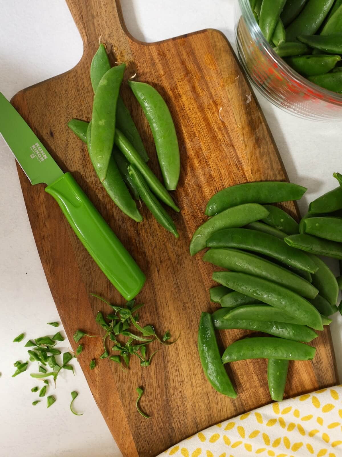 trimmed sugar snap peas on a board with a paring knife