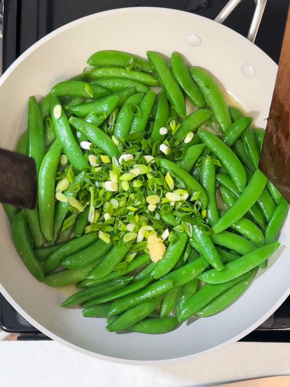 sliced scallions and garlic added to cooked sugar snap peas in a skillet