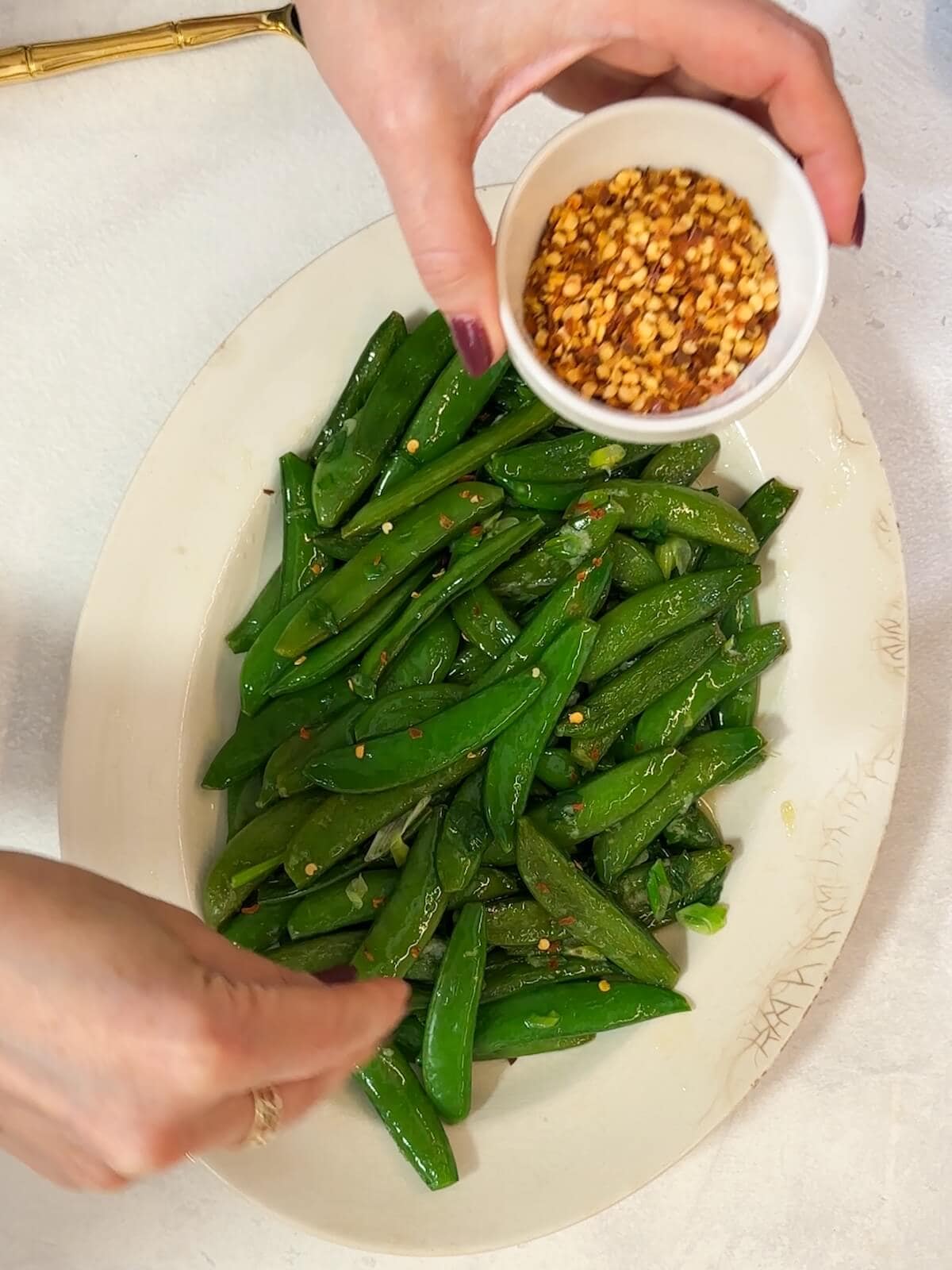 Adding seasonings and red pepper flakes to sugar snap peas