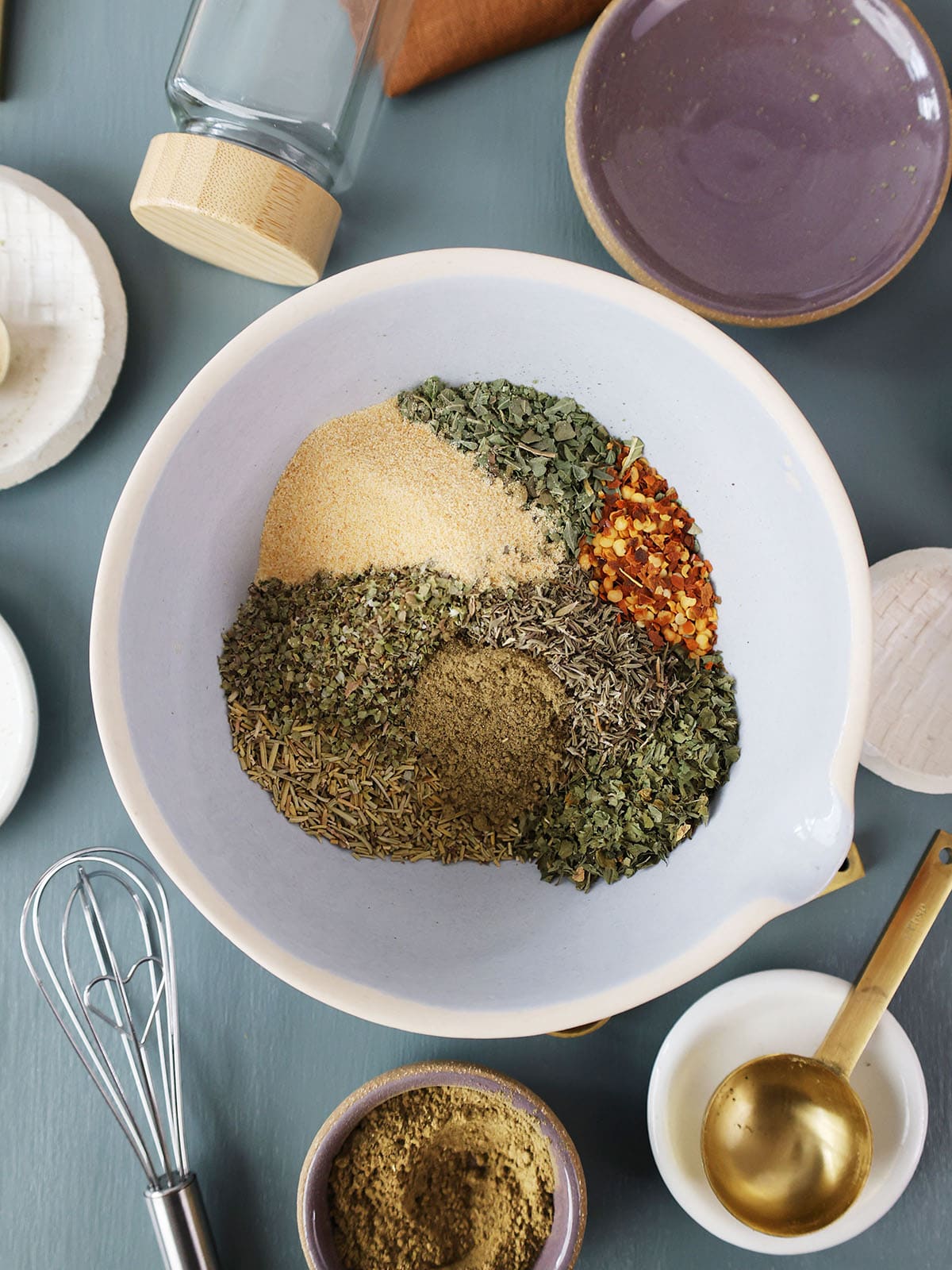 A bowl of seasonings next to measuring spoons, bowls, and containers.