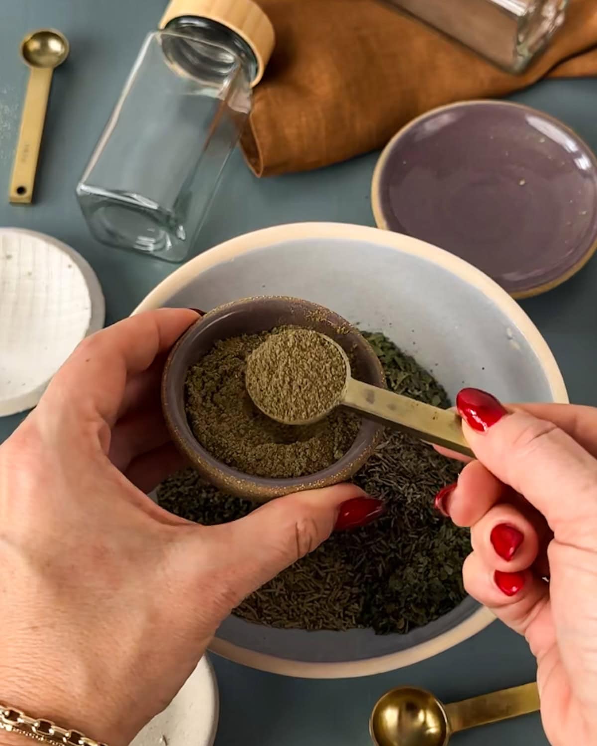 Measuring dried spices into bowl to make homemade Italian seasoning.