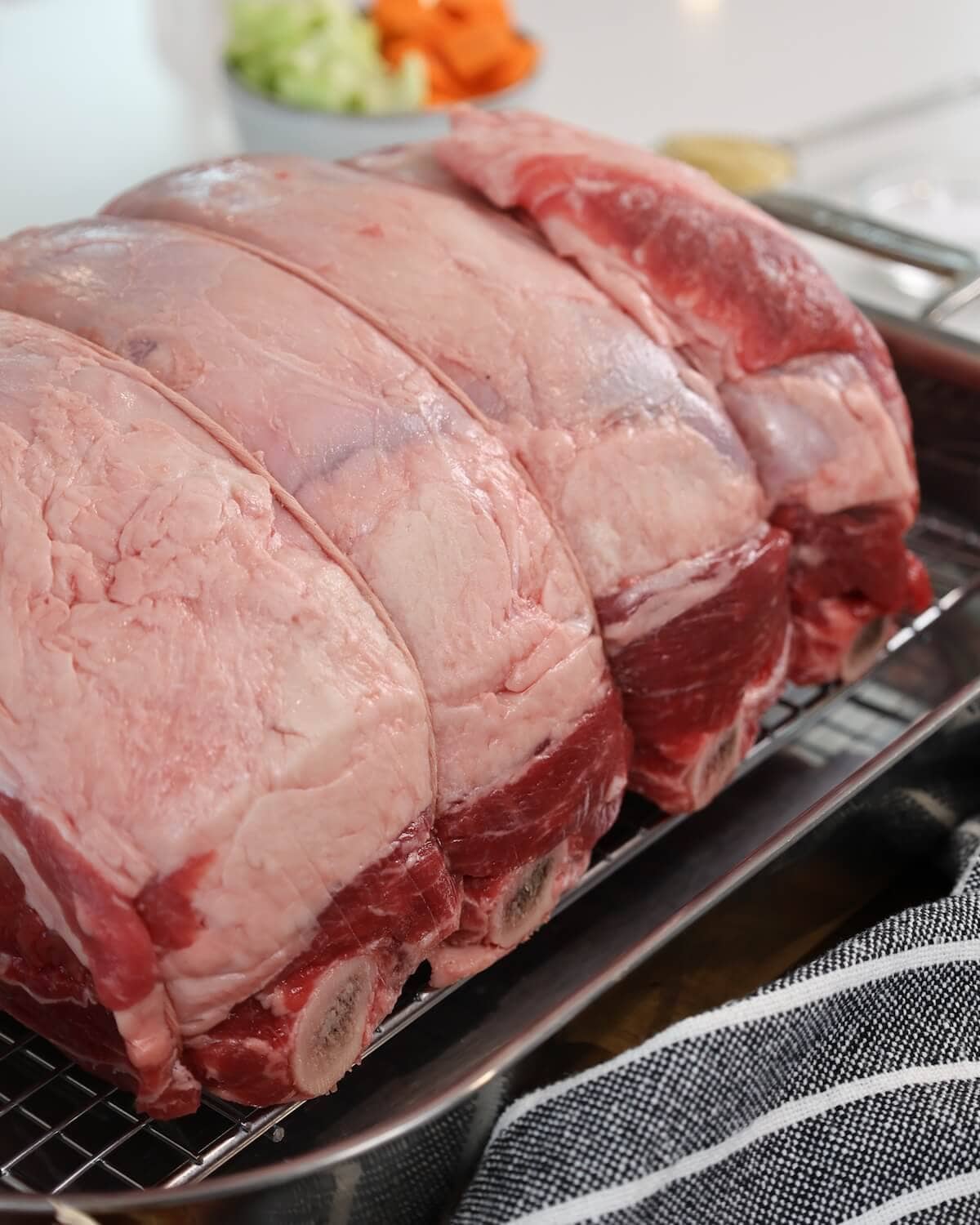 A close up of a large prime rib roast tied with kitchen twine sitting in a pan.