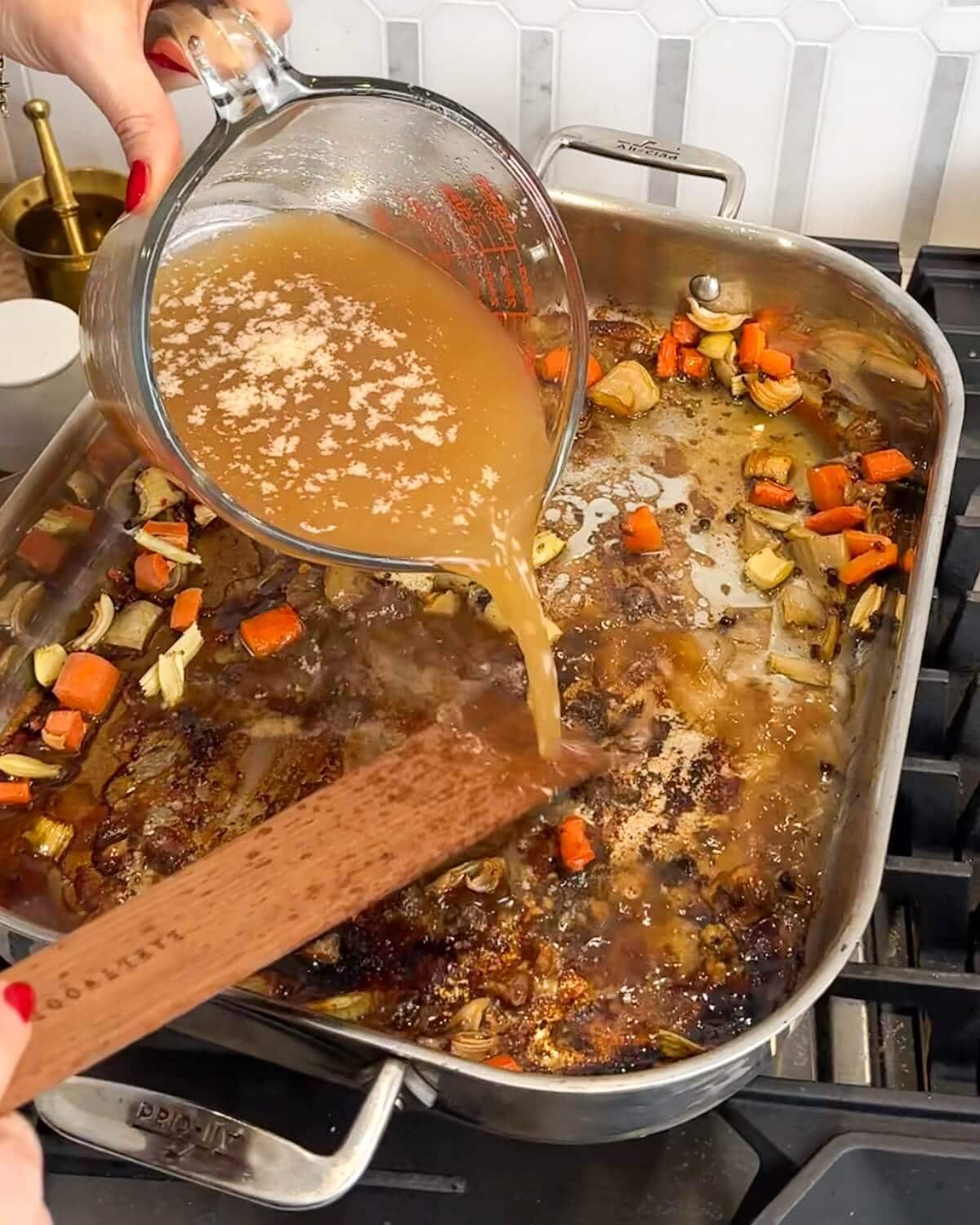 Pouring broth into roasting pan on the stove to deglaze the prime rib pan drippings.
