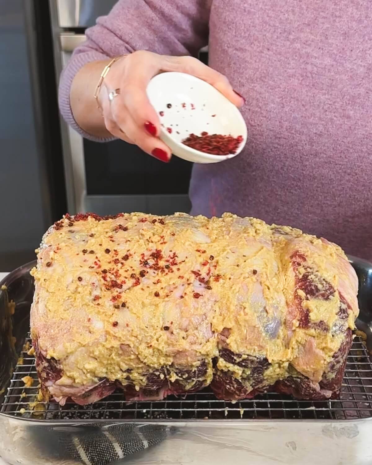 A raw prime rib roast sitting in a roasting pan, seasoned with pink peppercorns.