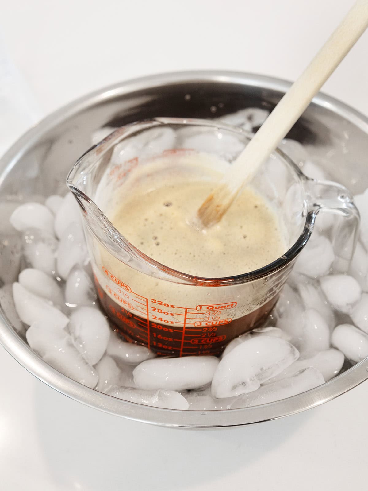 A measuring cup with browned butter in a bowl of ice cooling down.