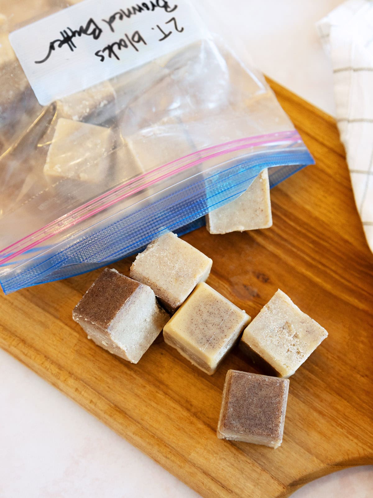Cubes of frozen browned butter spilling out of a plastic zipper bag onto a wooden cutting board.
