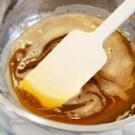 Close up of liquid browned butter in a silver bowl with a spatula in it.