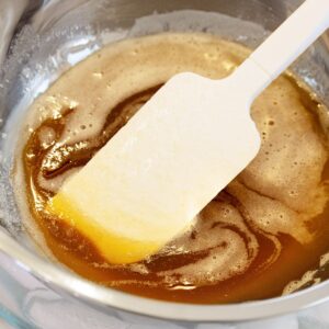 Close up of liquid browned butter in a silver bowl with a spatula in it.