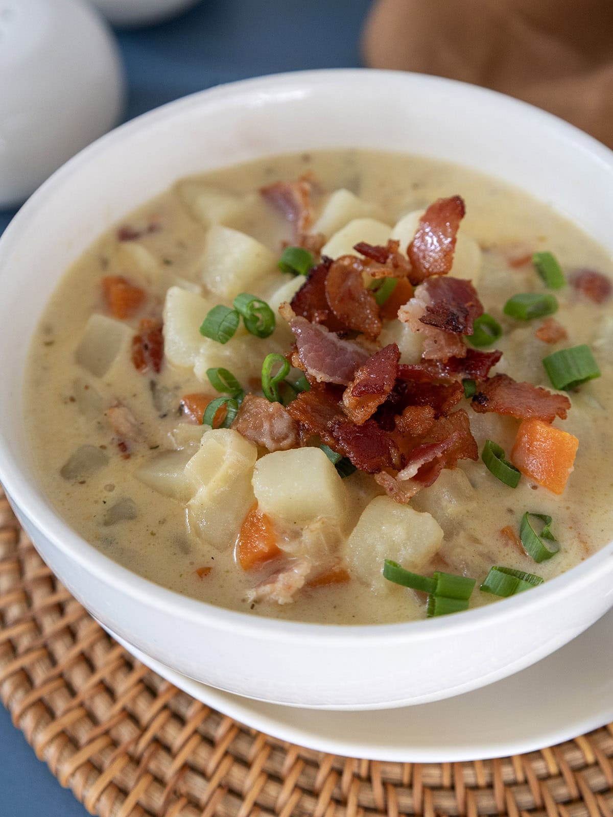 Close up of a bowl of potato bacon cheese soup topped with crispy bacon and sliced scallions.