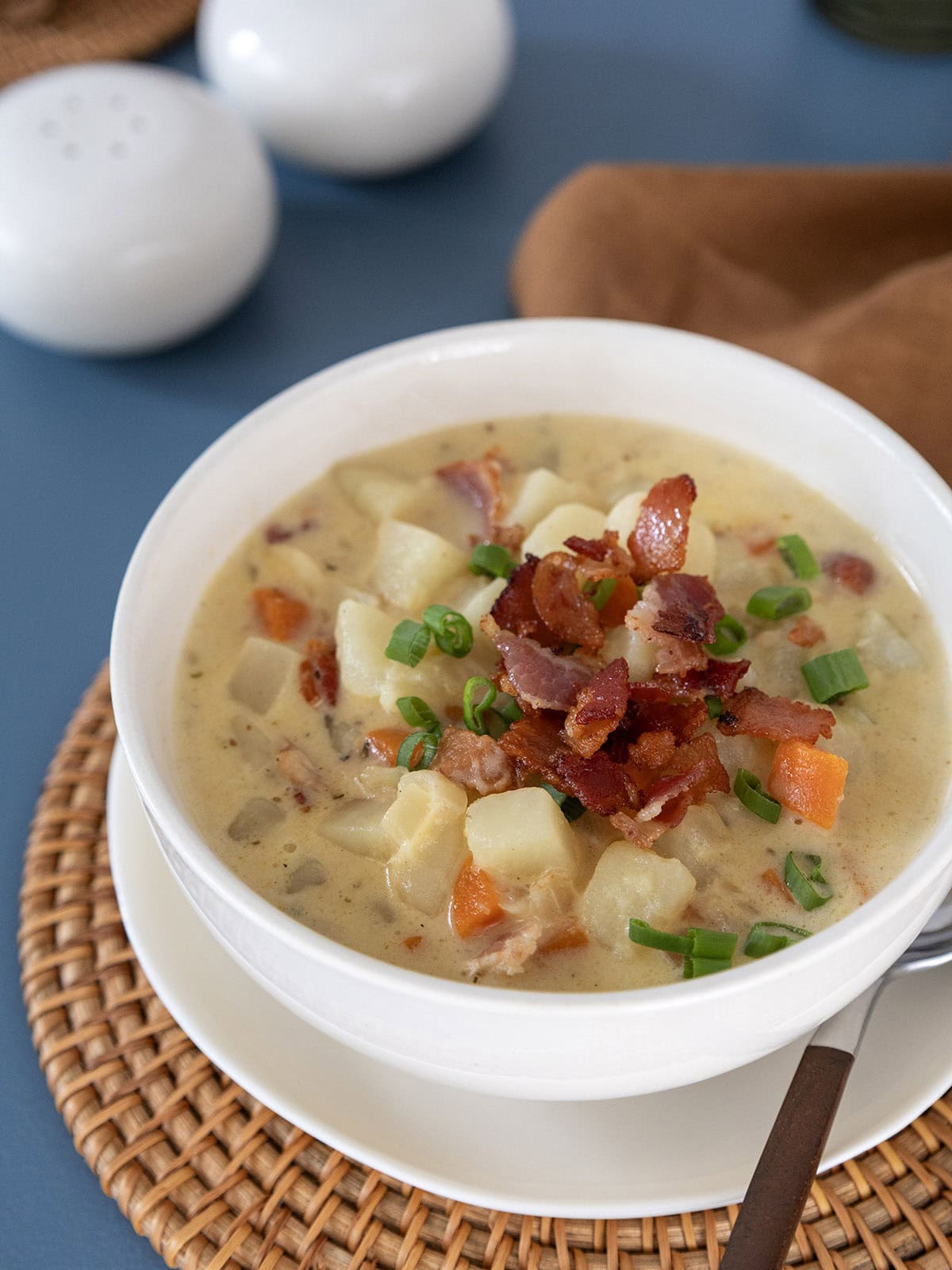 A bowl of potato bacon cheese soup topped with crispy bacon and sliced scallions.