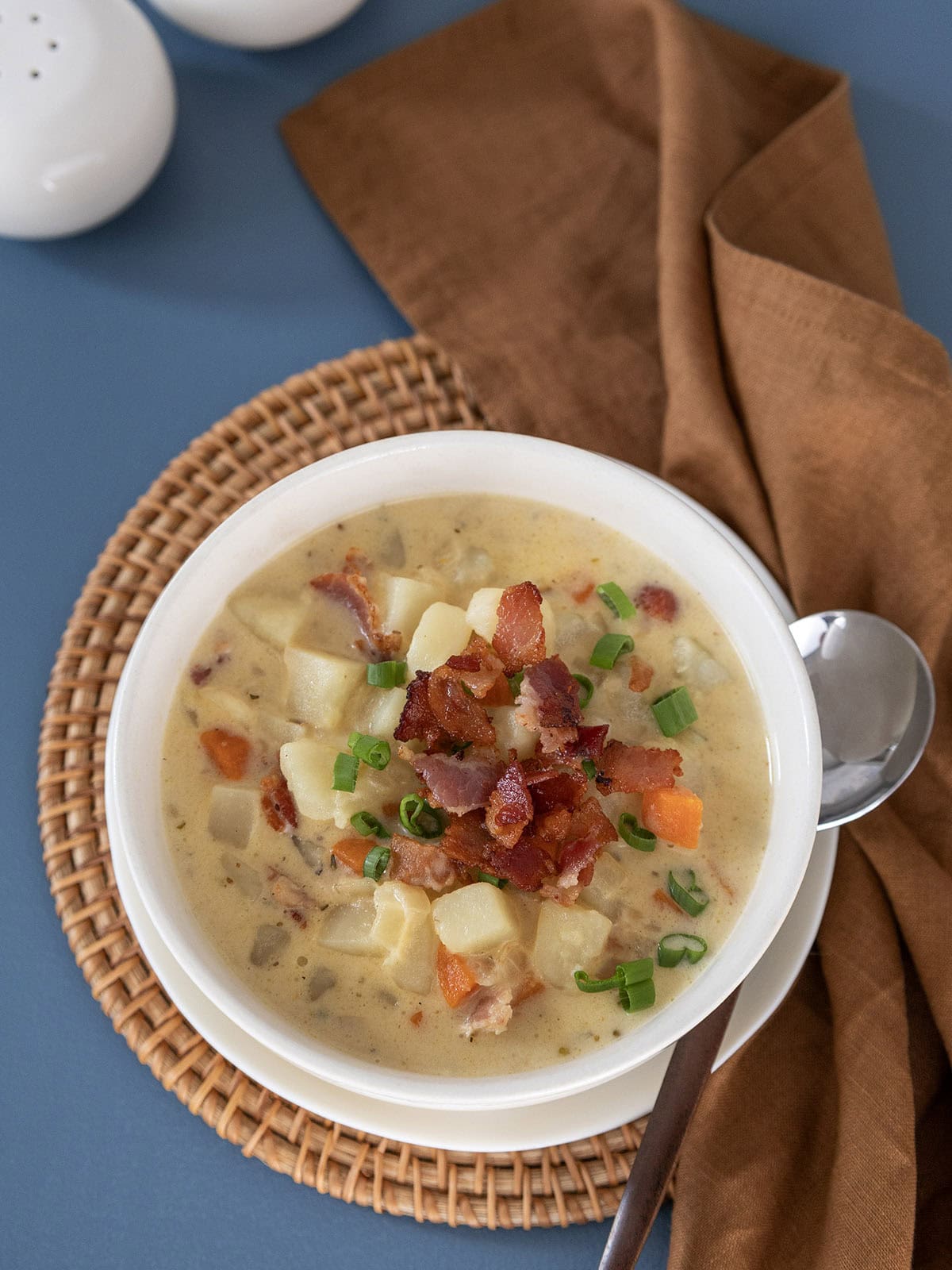 Top view of a bowl of potato bacon cheese soup topped with crispy bacon and sliced scallions.
