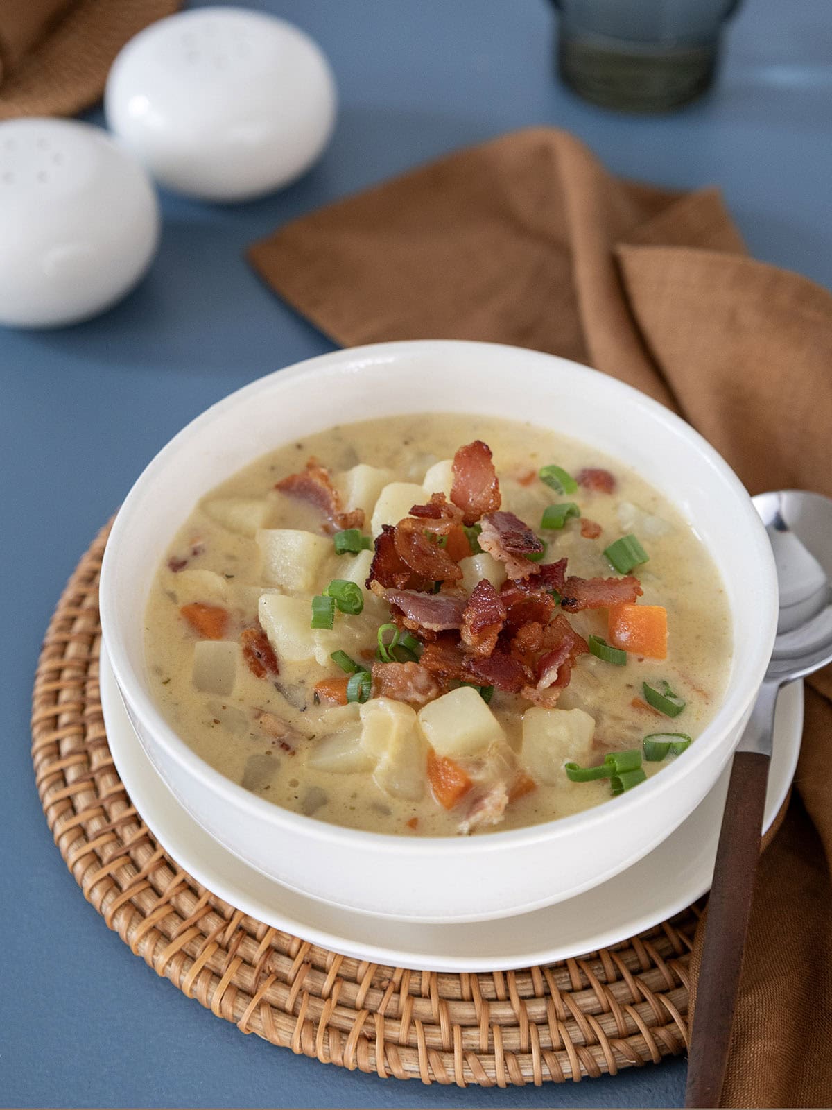 A bowl of potato bacon cheese soup topped with crispy bacon and sliced scallions.