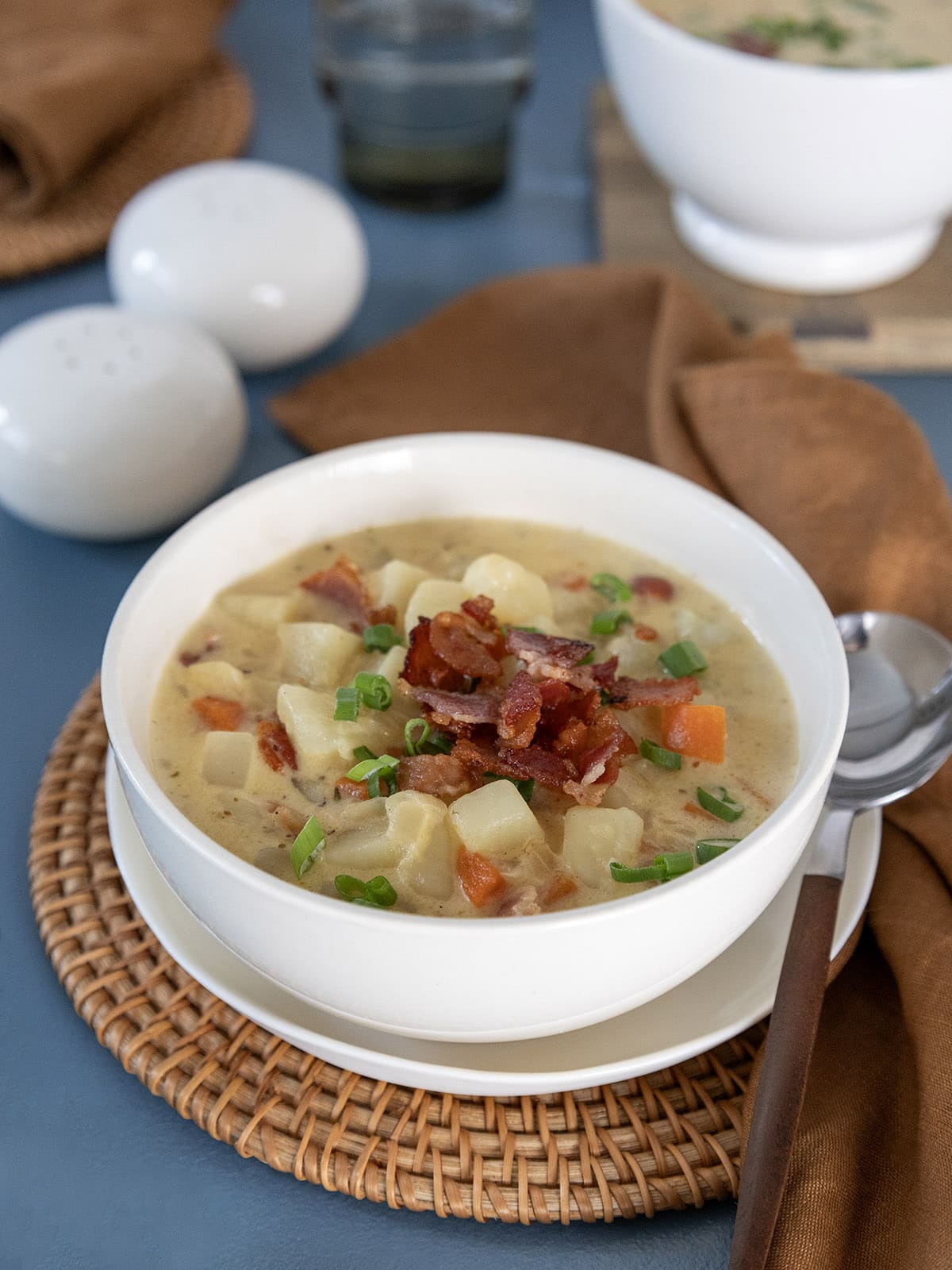 Close up of a bowl of potato bacon cheese soup topped with crispy bacon and sliced scallions.