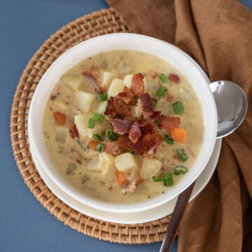 Top view of a bowl of potato bacon cheese soup topped with crispy bacon and sliced scallions.