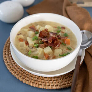 Close up of a bowl of potato bacon cheese soup topped with crispy bacon and sliced scallions.