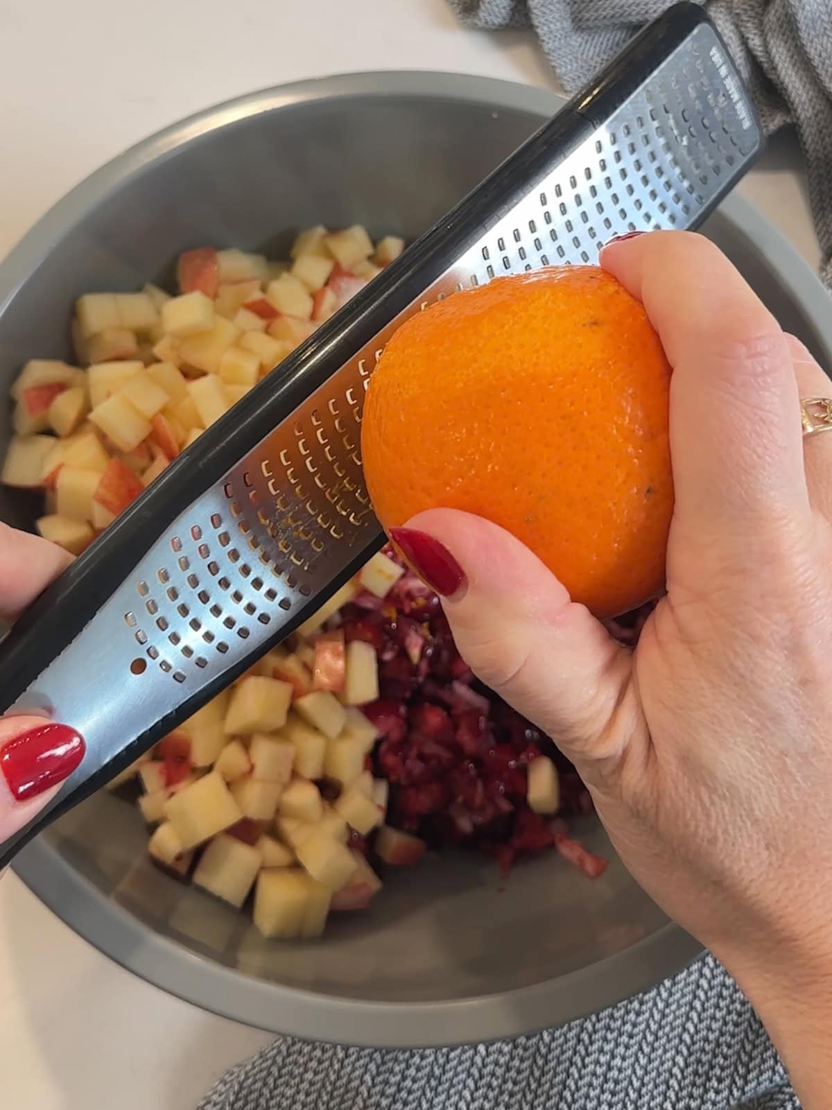 zesting an orange with a rasp over a bowl of relish.