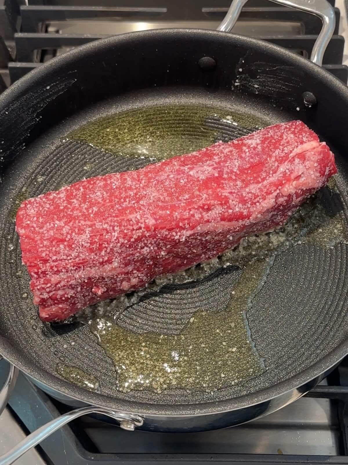 browning a beef tenderloin in a skillet with oil.