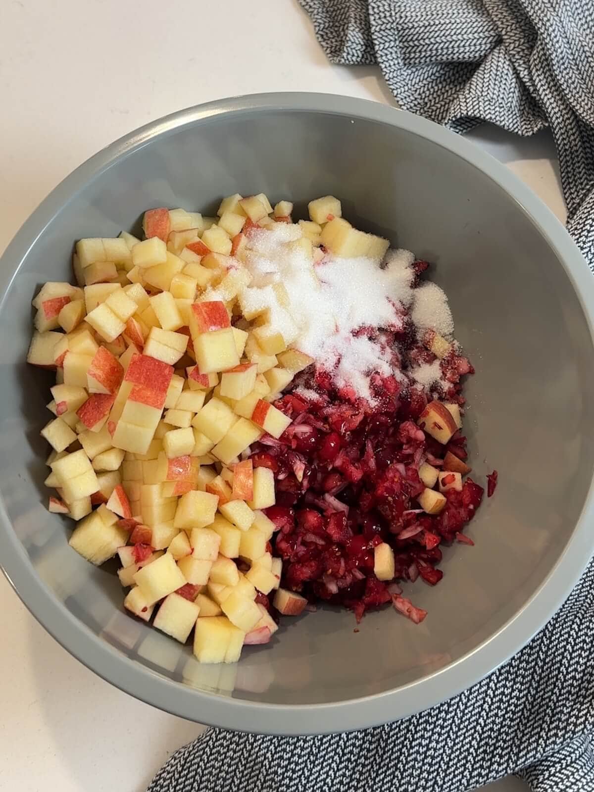 chopped cranberries in a bowl with diced apples and sugar for cranberry relish