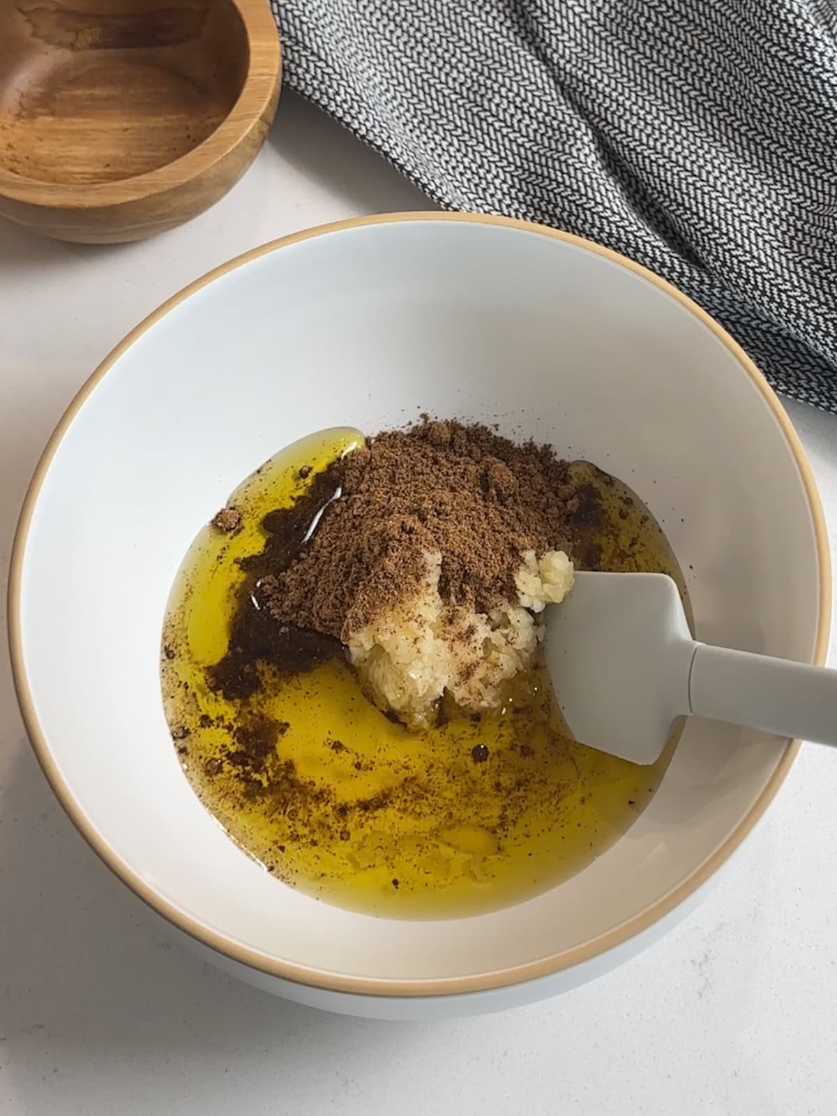 white bowl with spatula filled with ingredients for beef tenderloin rub, including olive oil, garlic, and spices.