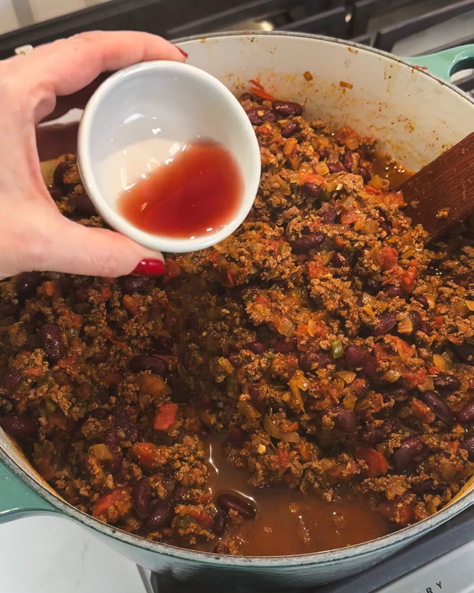Adding red wine vinegar to chili to enhance flavor.