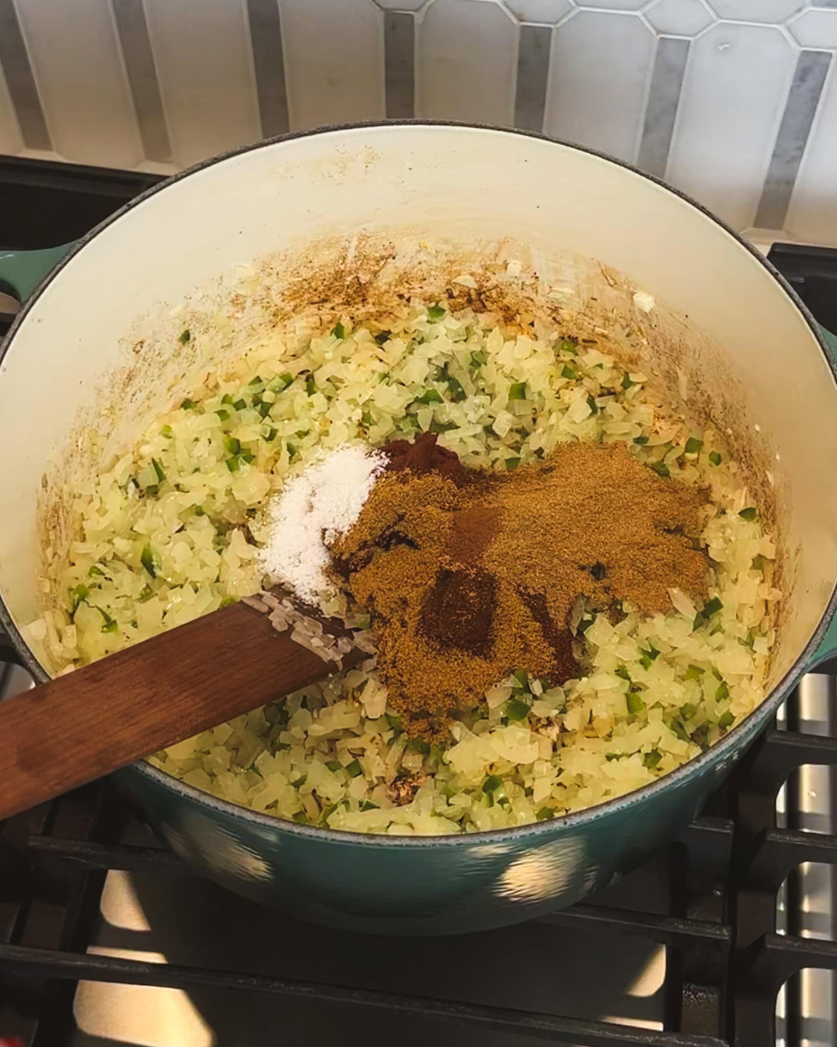Adding spices and salt to a large pot of sauteed onions for chili.