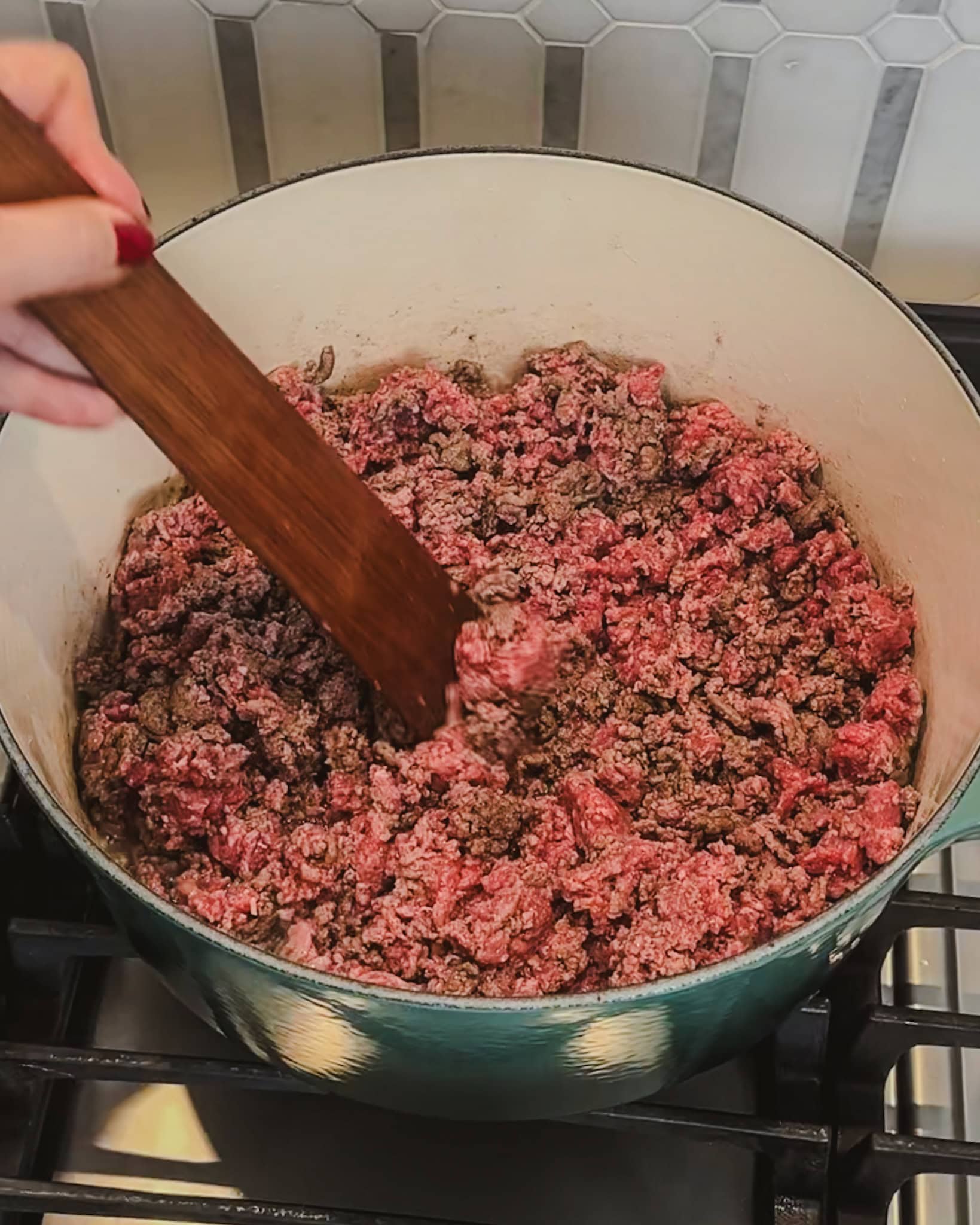 browning ground beef in a large pot using a wooden spatula.
