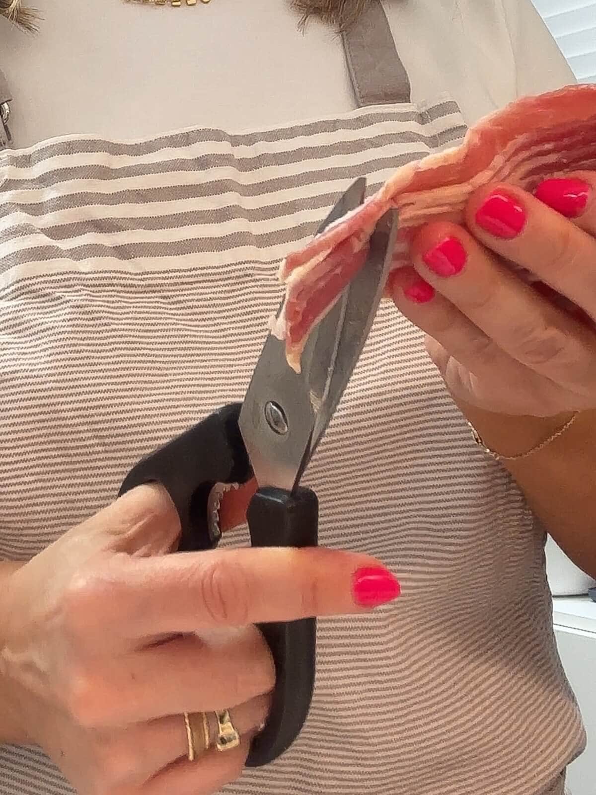 Hand cutting bacon with kitchen scissors. 