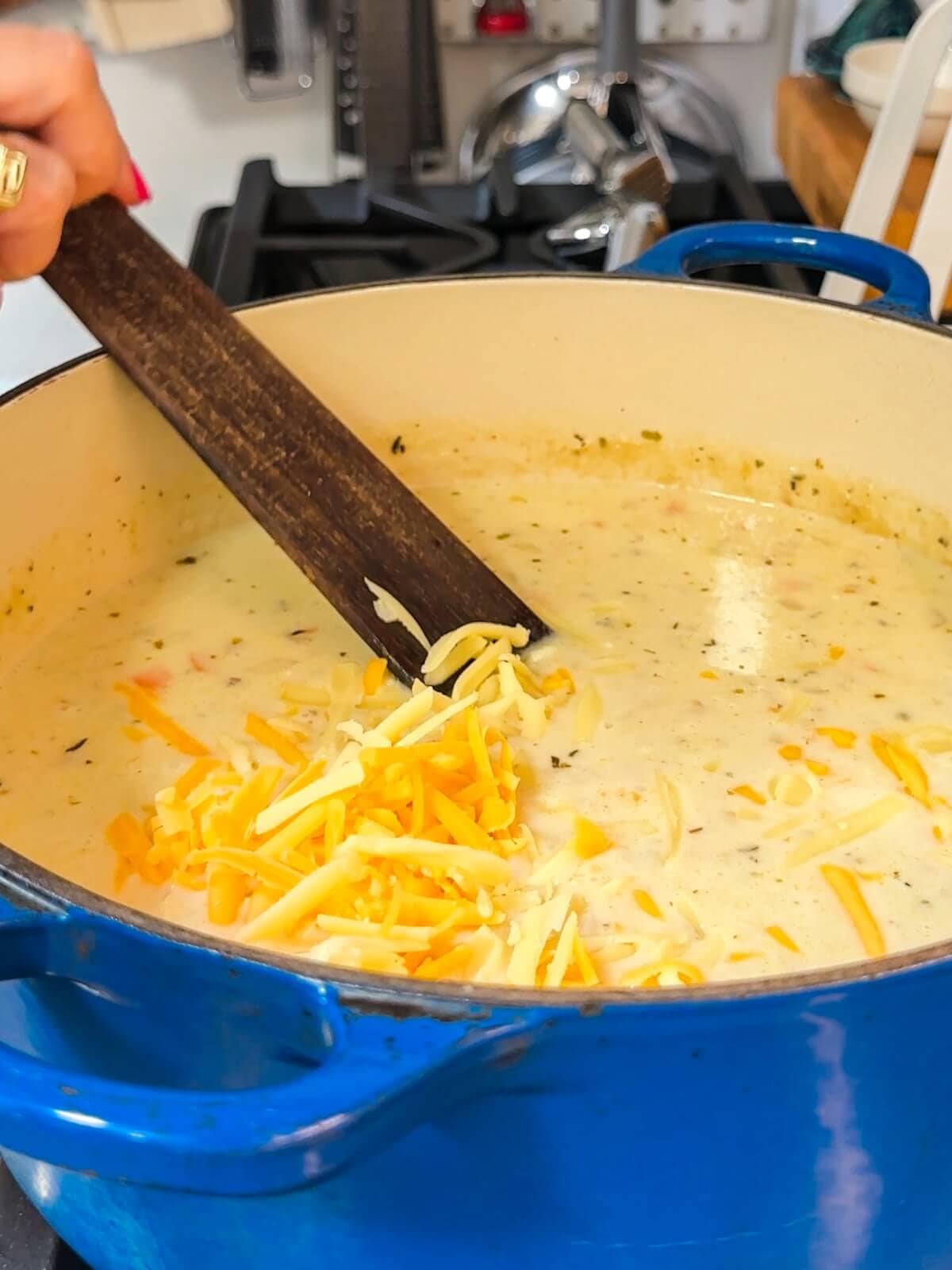 Adding grated cheese into a pot of potato soup to melt.