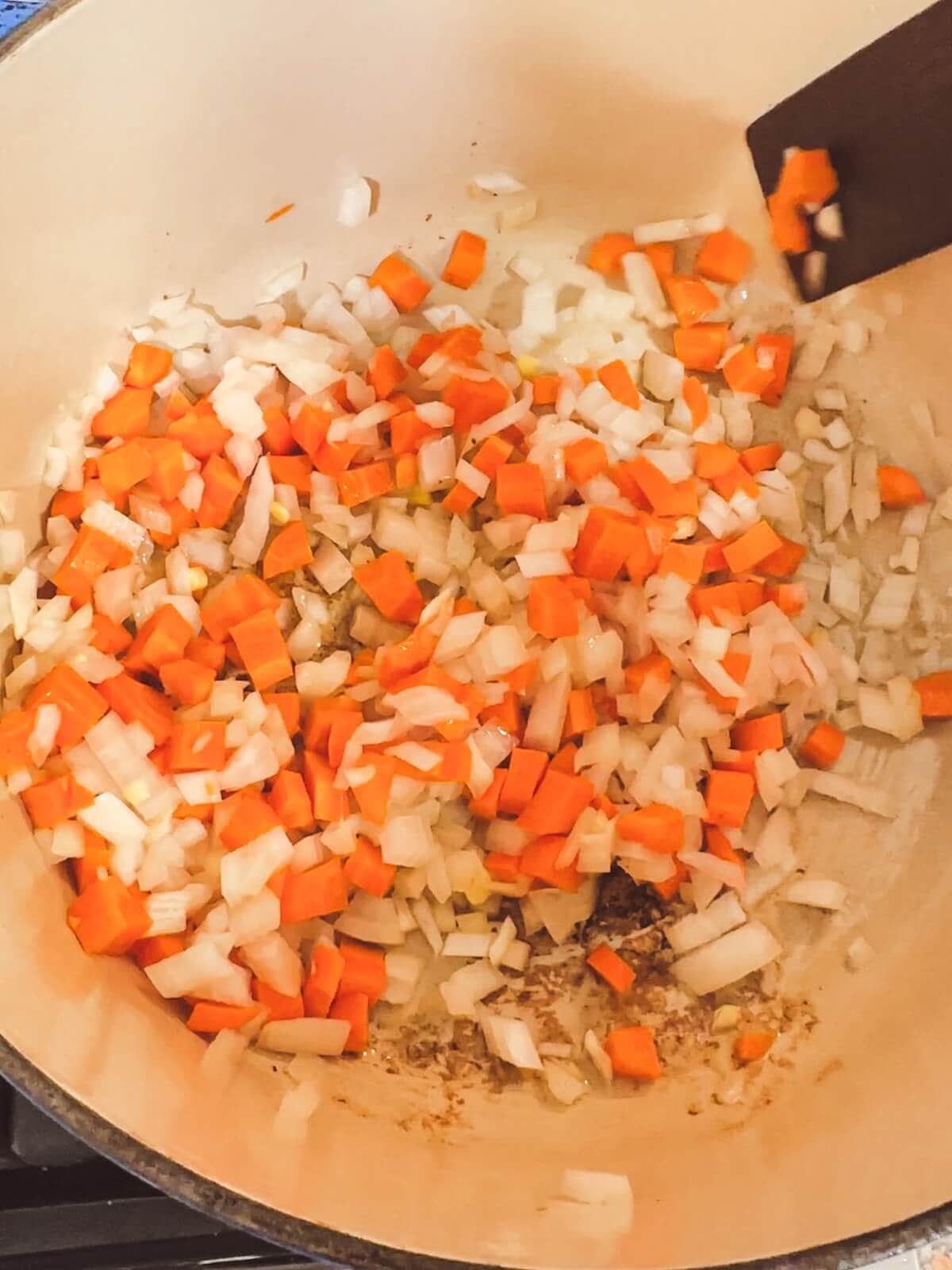 Carrots, onions, and garlic being added to a soup pot. 