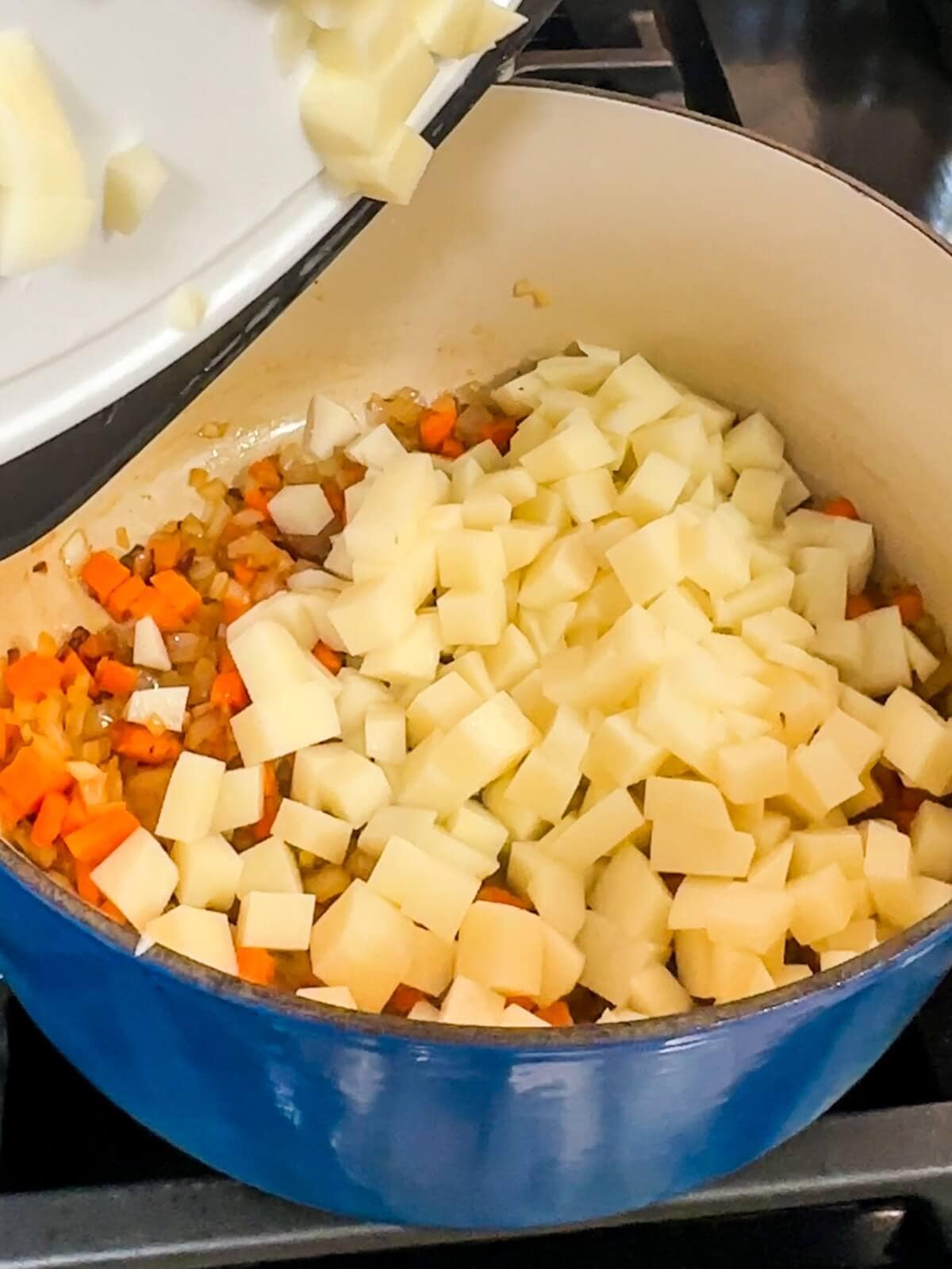 Diced potatoes being stirred into a pot to make potato soup.