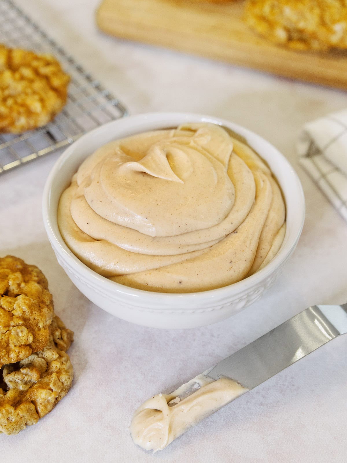 A white bowl of browned butter frosting next to cookies and a knife.