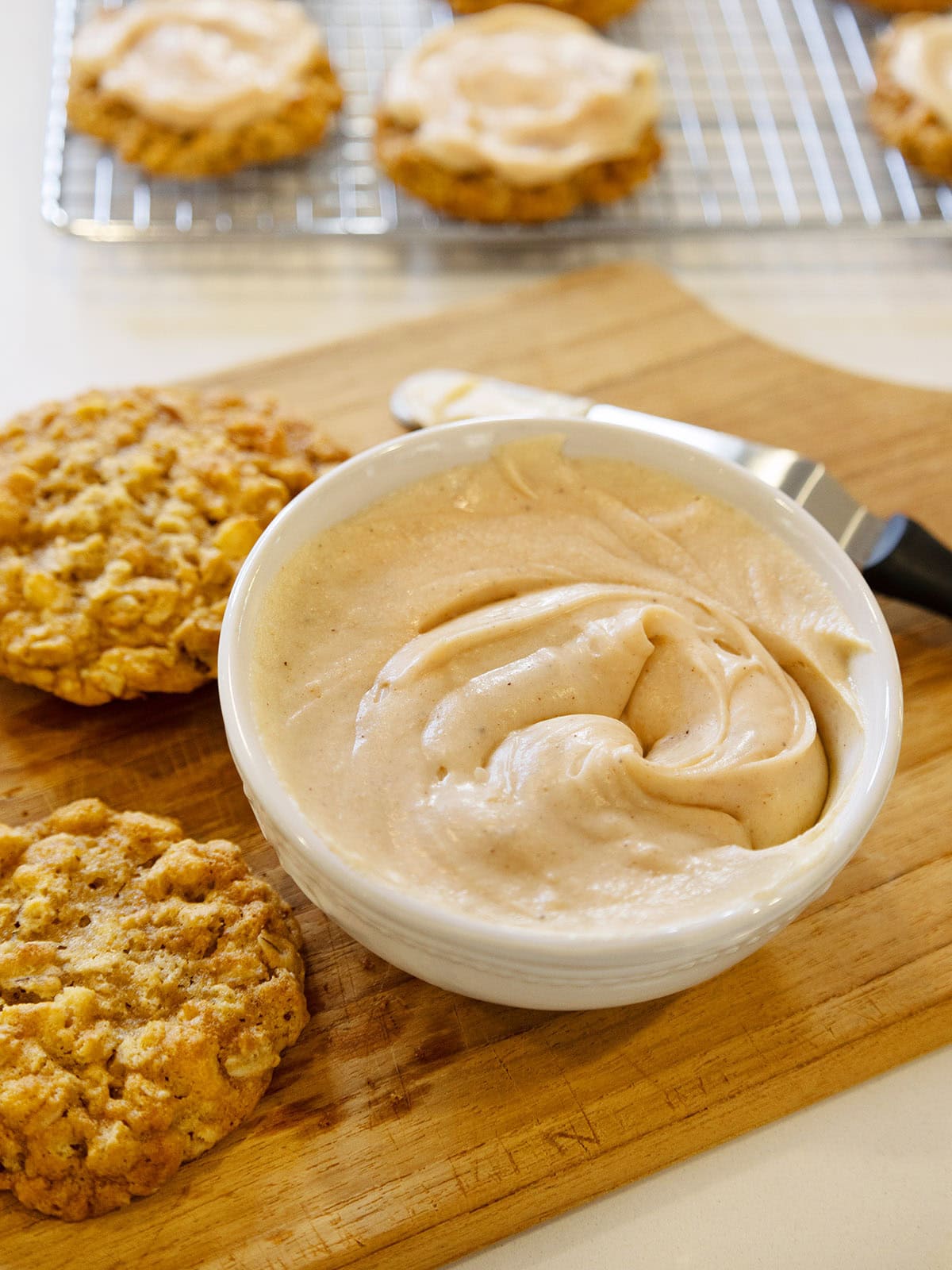 A bowl of browned butter frosting next to some cookies.