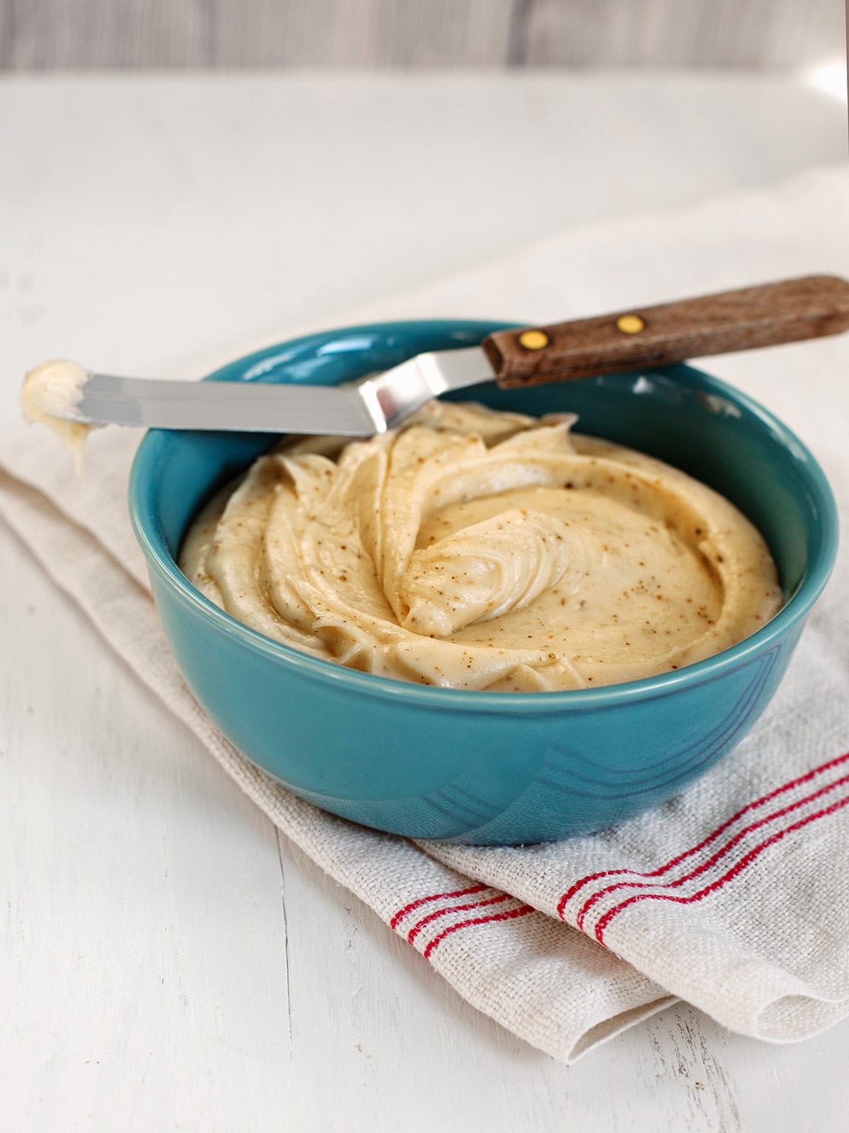 A teal bowl of browned butter frosting with an offset spatula resting on top.