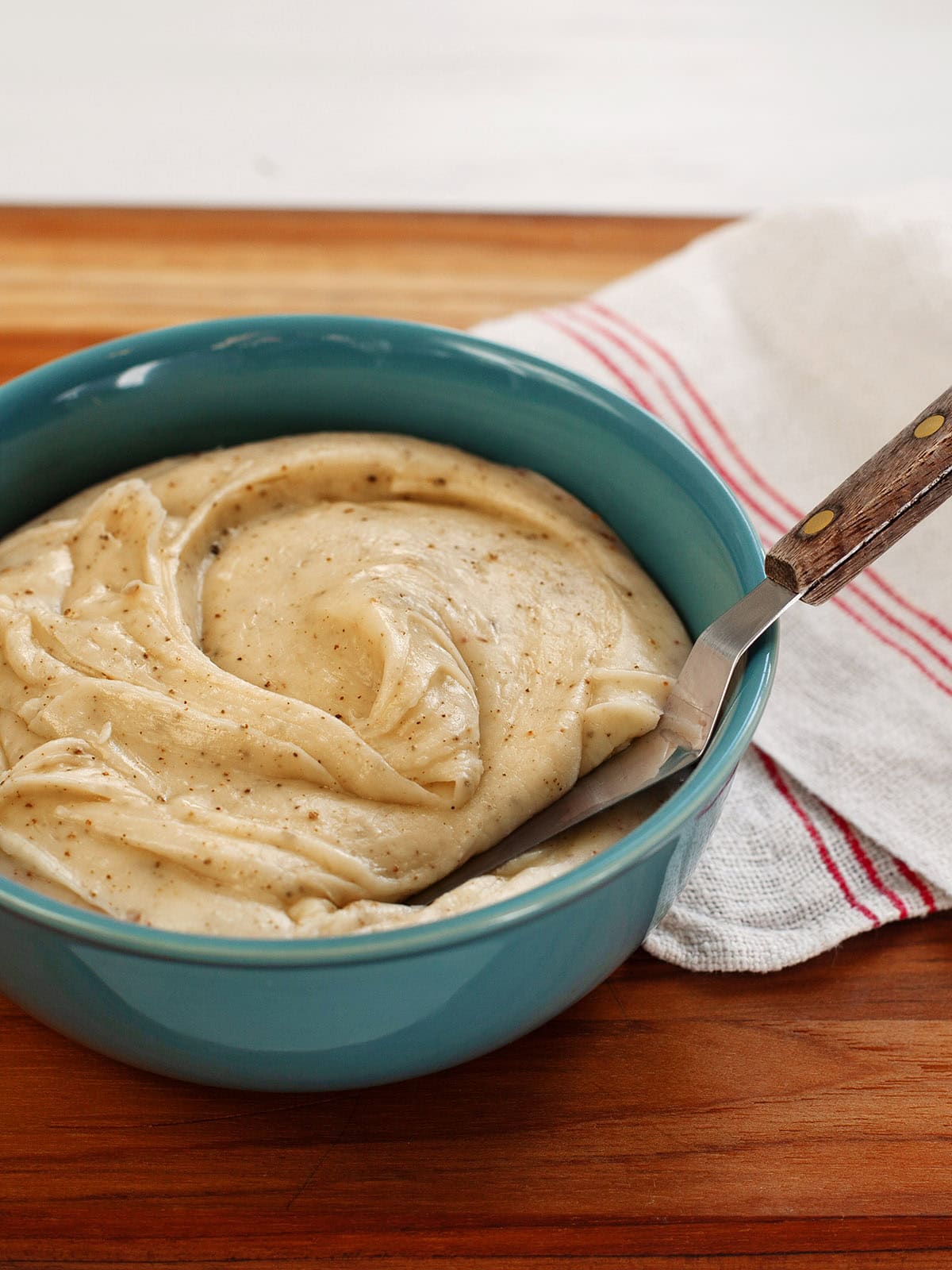 A teal bowl of browned butter frosting with a spatula in it.