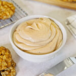 A bowl of browned butter frosting next to cookies.