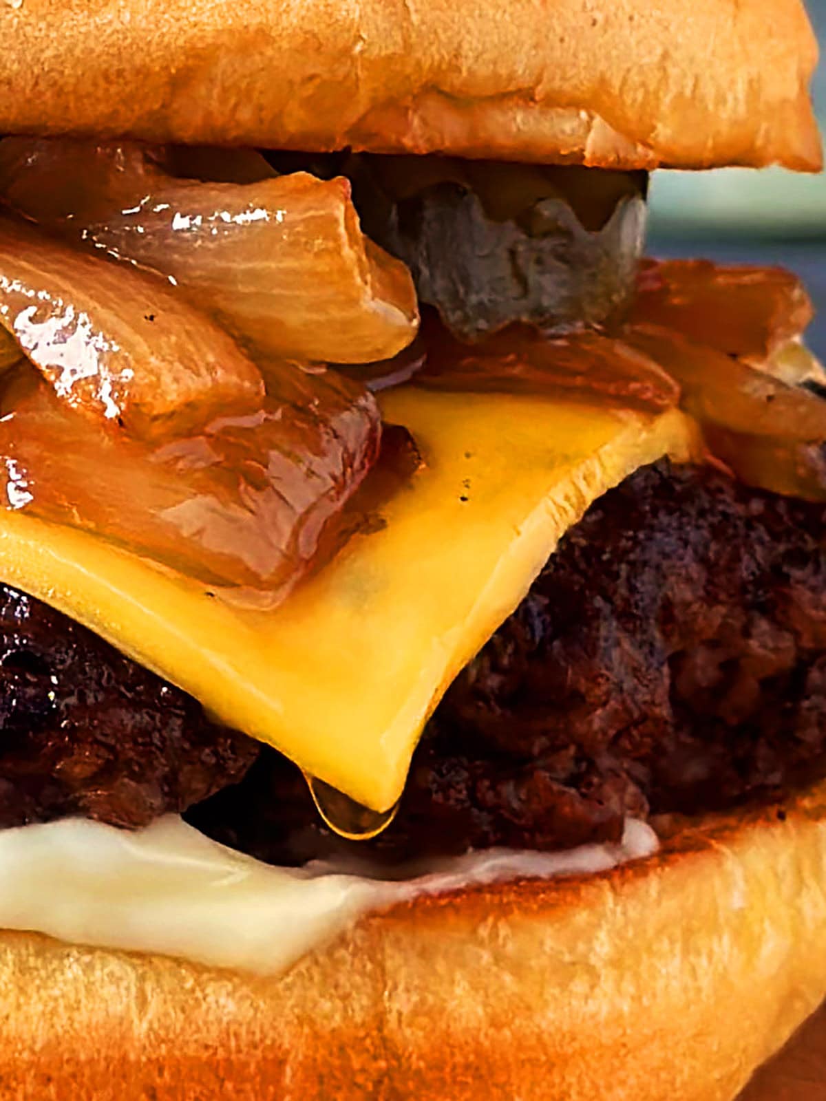 Close up of a butter burger topped with cheese, onions, and pickles. 