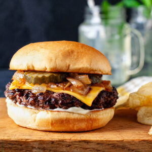 Close up of a butter burger on a wooden surface with a mason jar in the background.