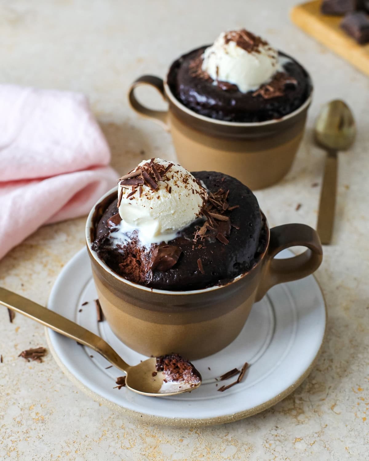 Two chocolate mug cakes with a bite removed out of front cake.