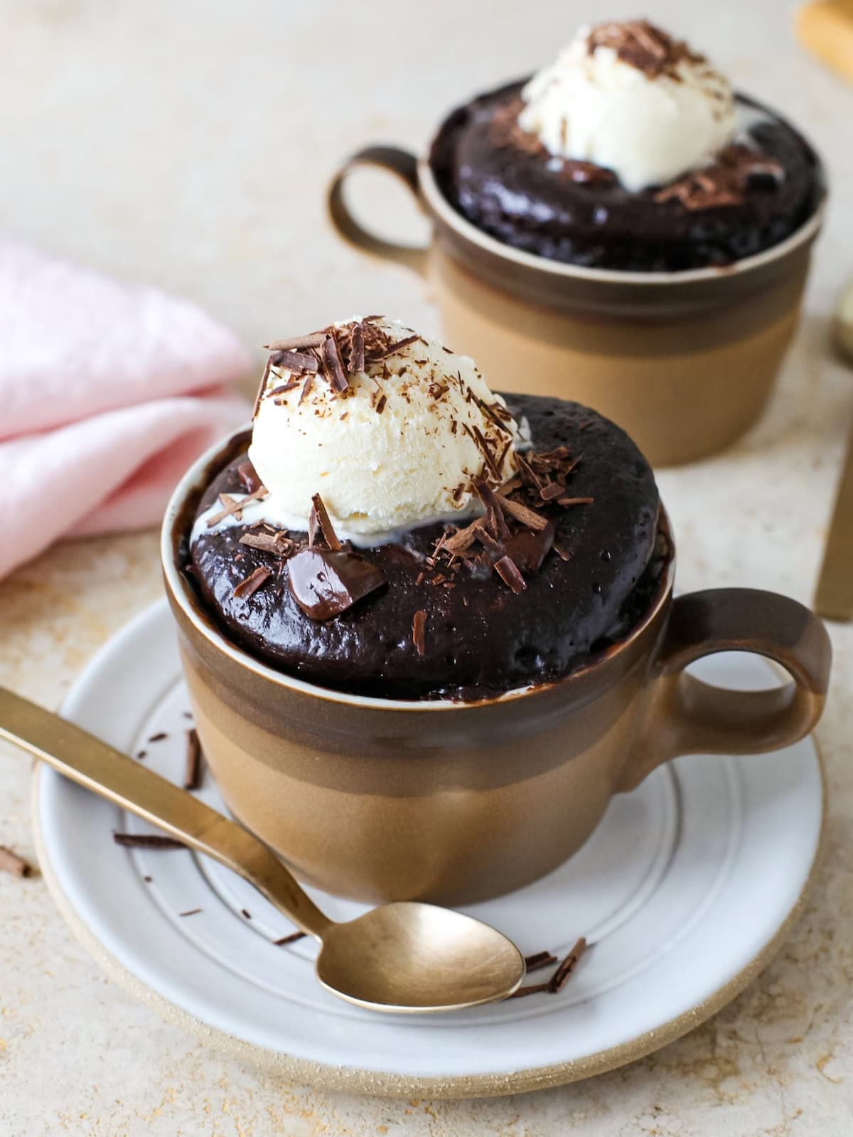 Two chocolate mug cakes with ice cream melting on top.