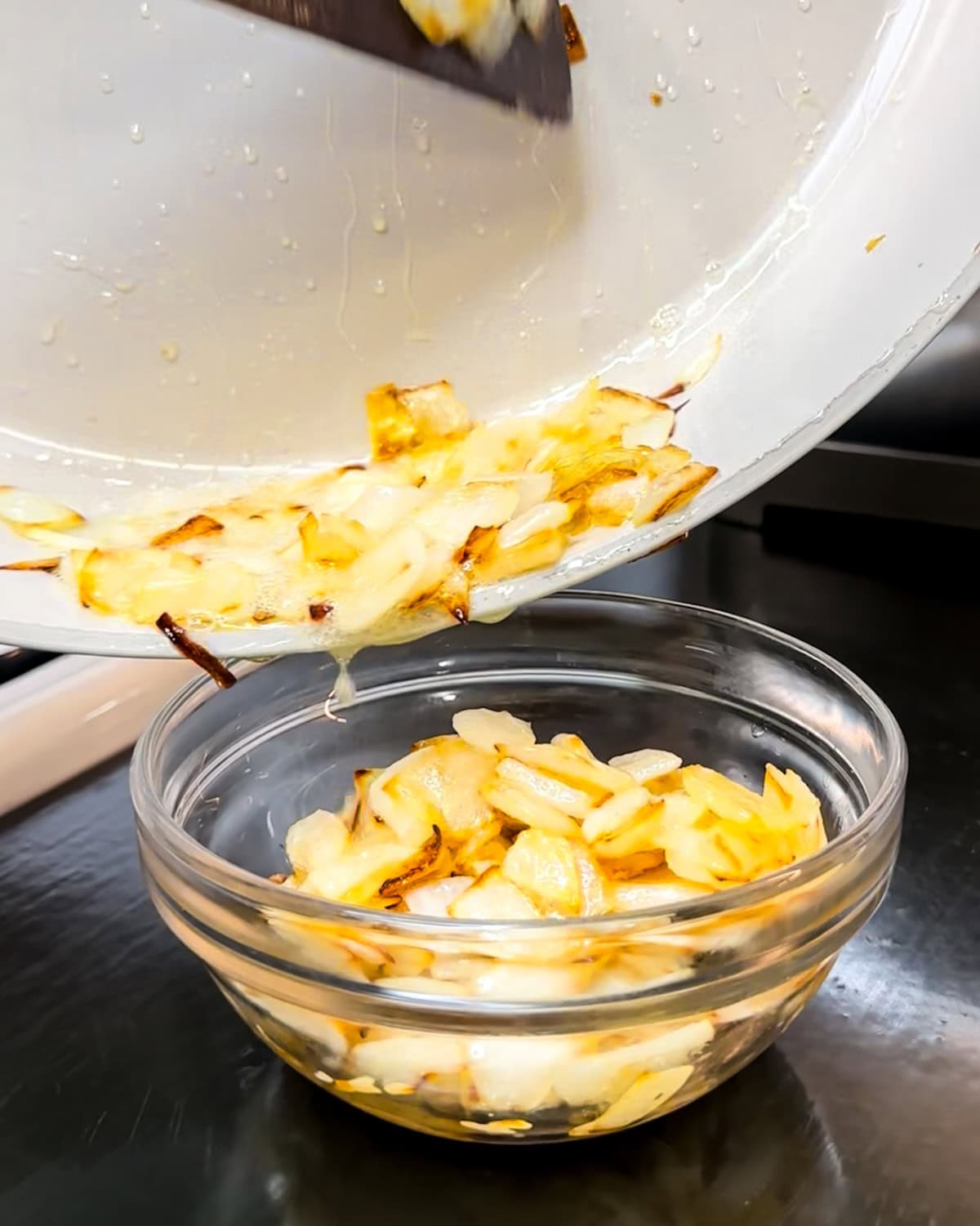 Onions being scooped into a bowl after being cooked. 