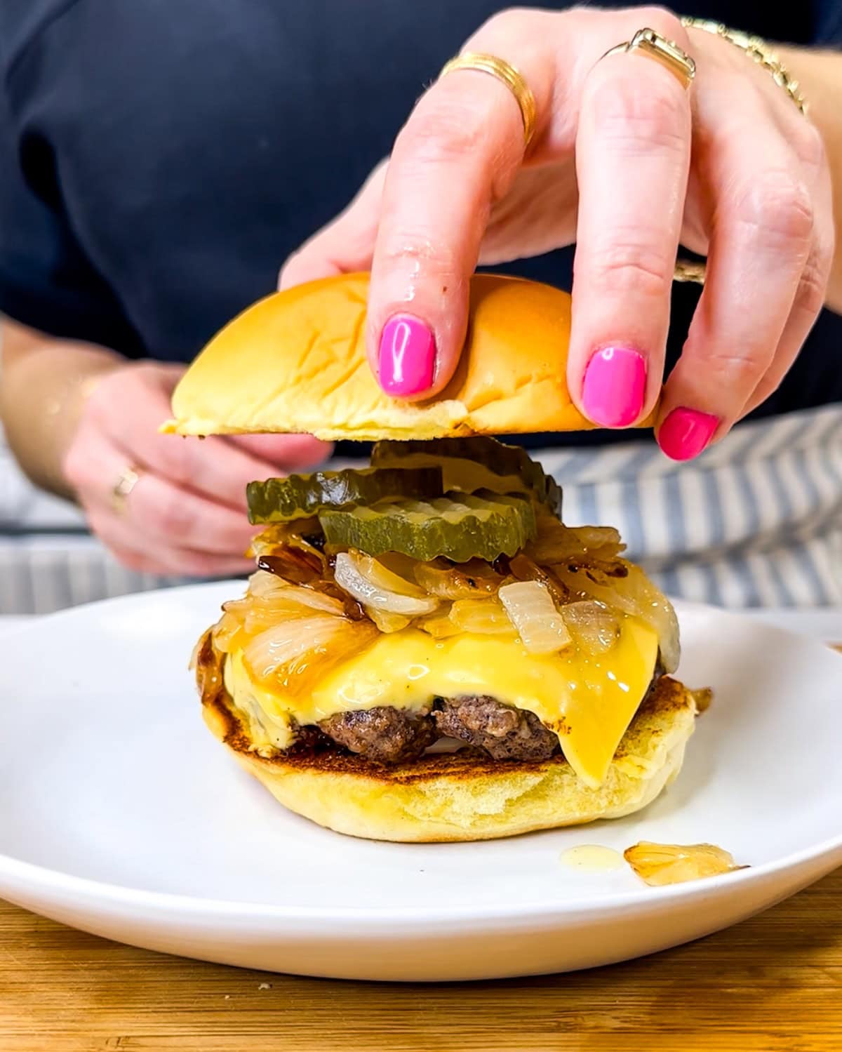 Hand placing top bun on a finished butter burger. 