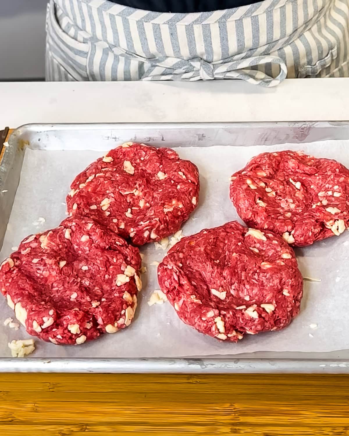 Four shaped butter burger patties on a parchment-line baking sheet. 