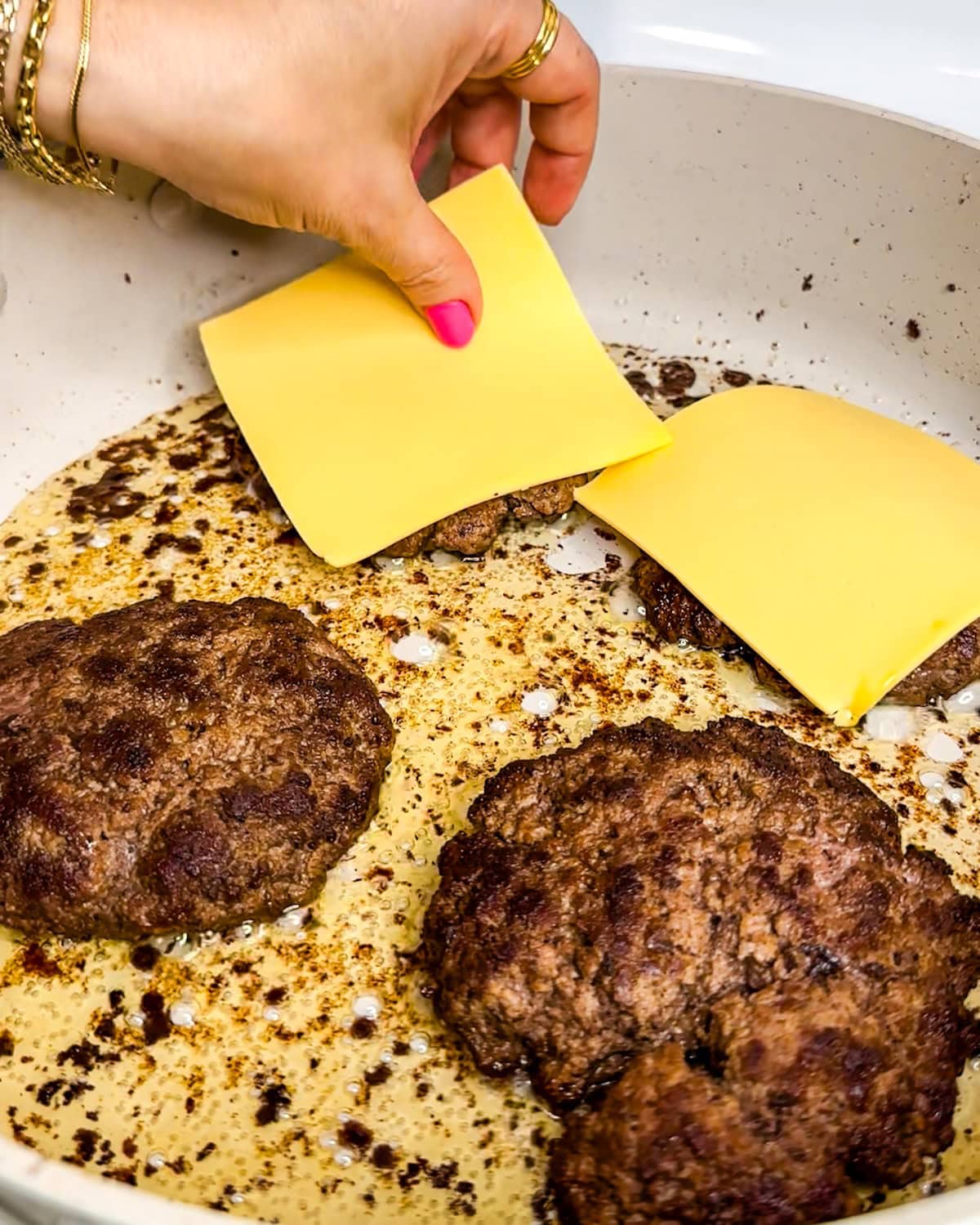 Placing cheese on top of butter burgers in a frying pan.